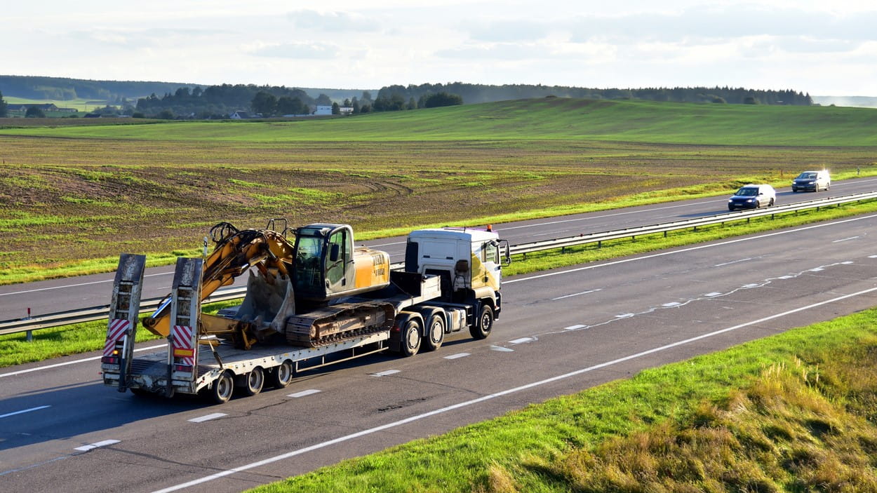 Lastebil lastet med gravemaskin kjører på motorvei.